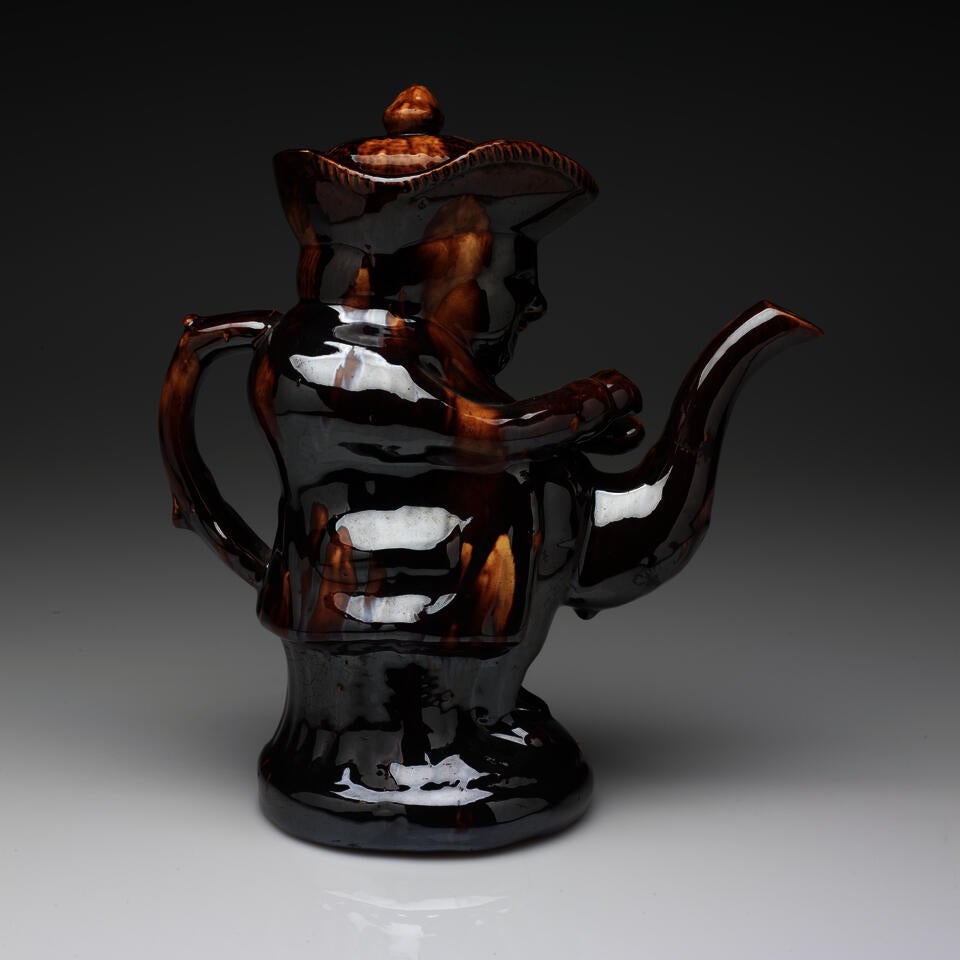 A dark brown teapot in the shape of a figure wearing a hat.