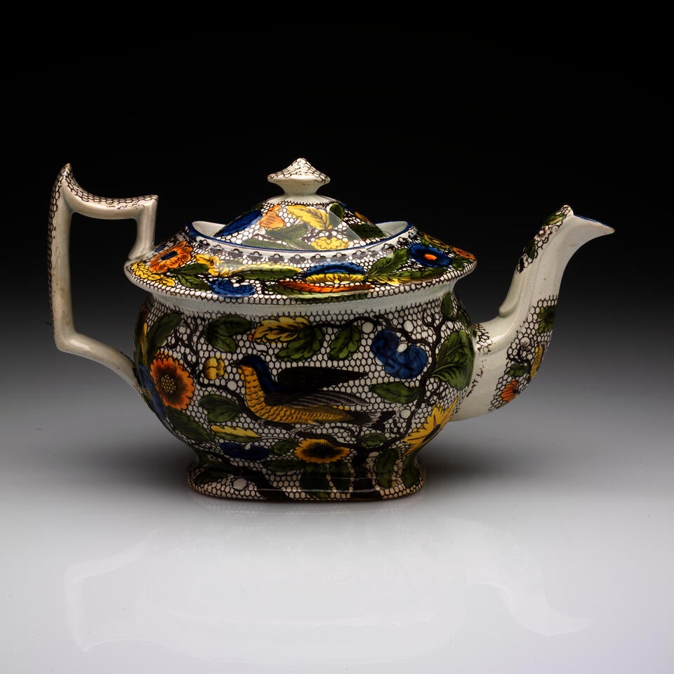 An angular transfer-printed earthenware teapot with white, black, yellow, green, and blue decorations.
