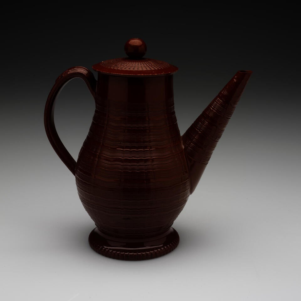 A brown stoneware coffee pot with a long straight spout, handle, foot, and lid with decorative horizontal grooves and projecting grooves. The final which is spherical in shape.