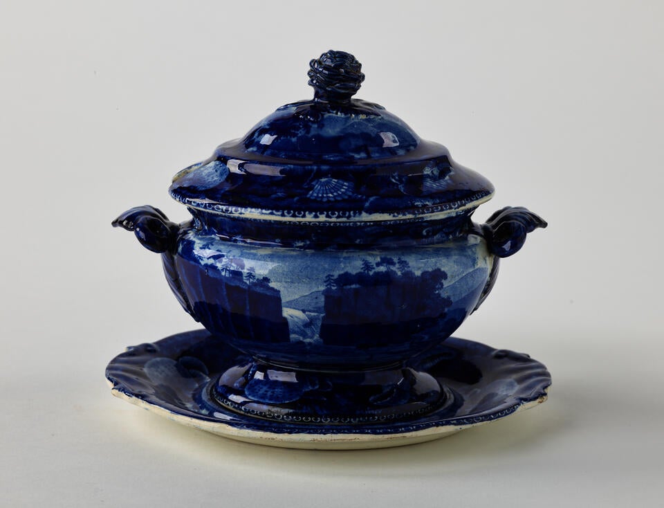A dark blue decorative sauce boat, two symmetrical sculptural handles that depict a bird’s head, foot, and lid with rounded finial 