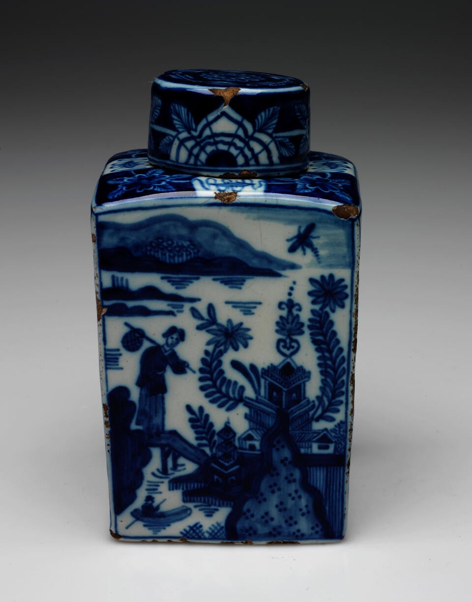 A rectangular vessel with blue and white architectural, landscape, and floral decorations. The lid is circular and has floral decorations as well. 