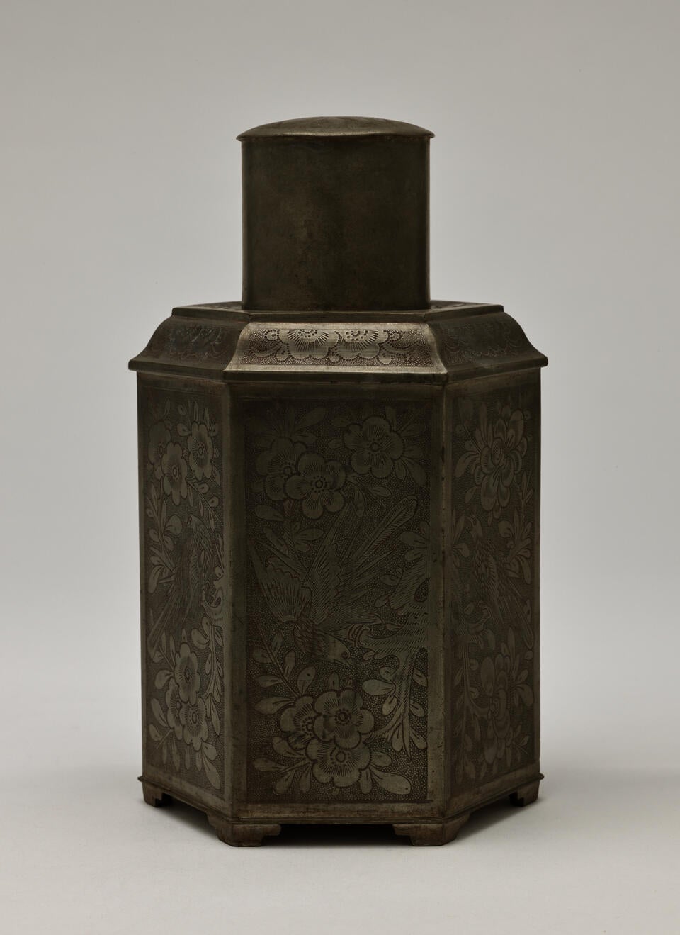 A pentagonal pewter tea caddy with floral decorations.