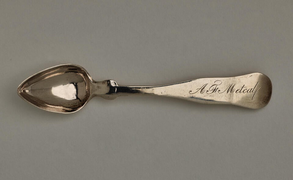  A silver salt spoon the bowl comes to a pointed tip, the neck is thin, and the handle is thicker and rounded at the end. 