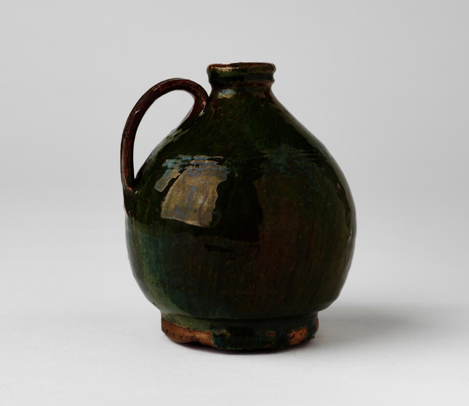 A short green bulbous jug with a tight rim, handle, and foot. 