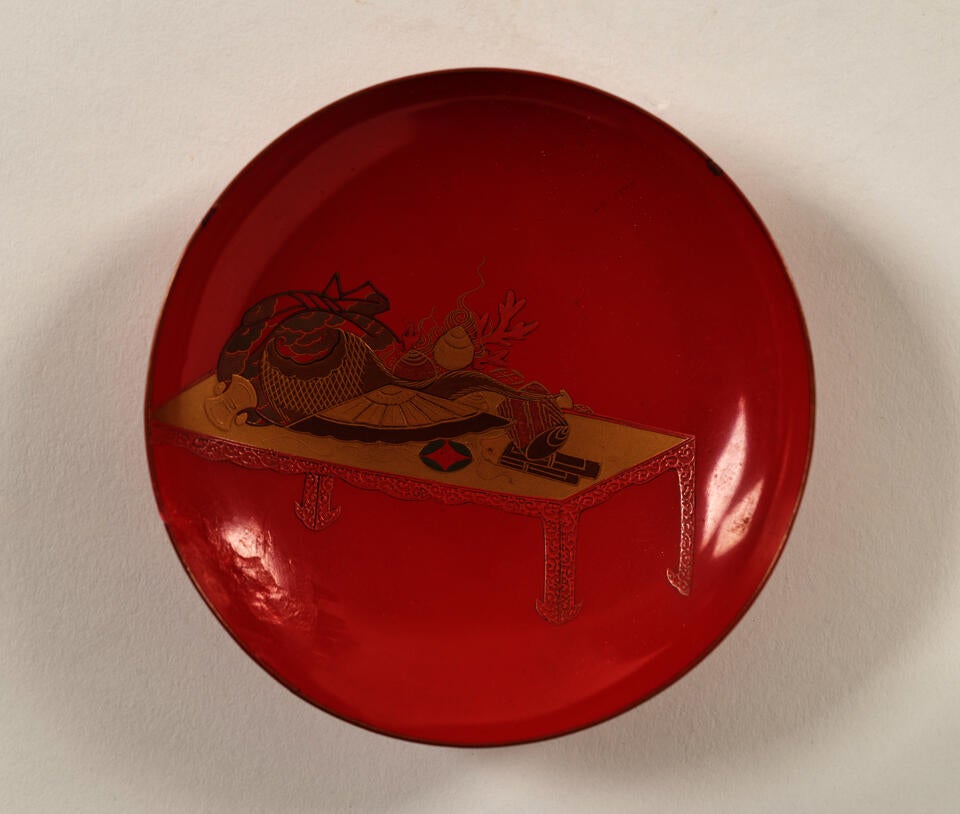 A lacquered wood wine cup that is bright red and has gold decorations. 