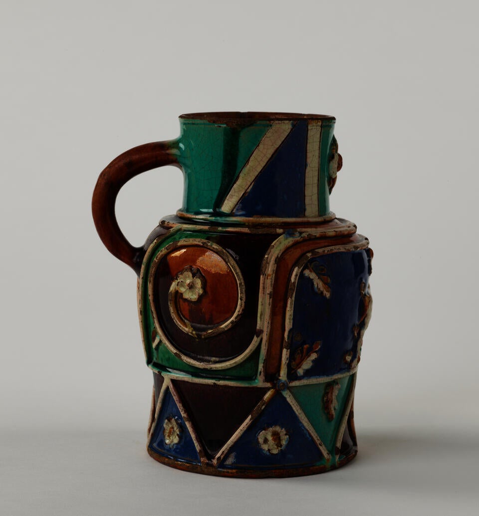A lead-glazed earthenware pitcher with white, blue, turquoise, orange, and black decorations. Some of the white decorations are raised. 