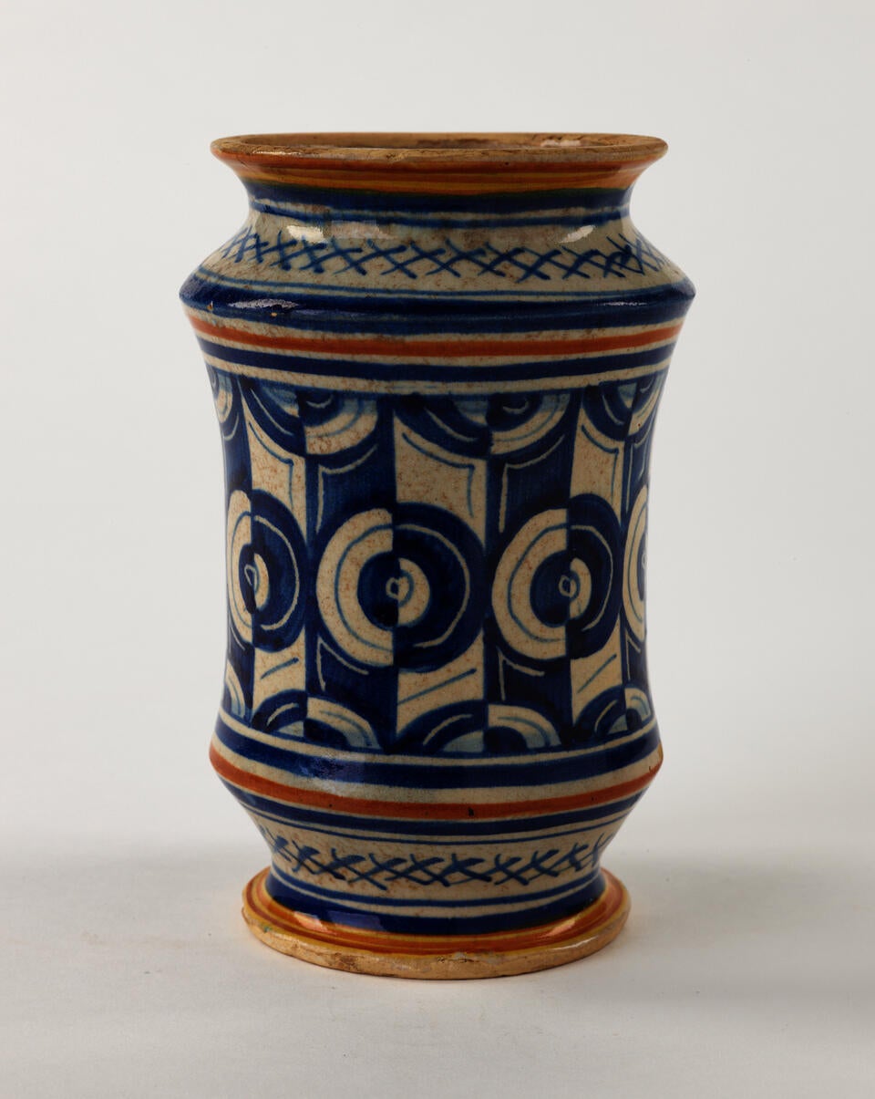 A tin-glazed earthenware jar that has white, orange, and blue symmetrical decorations.