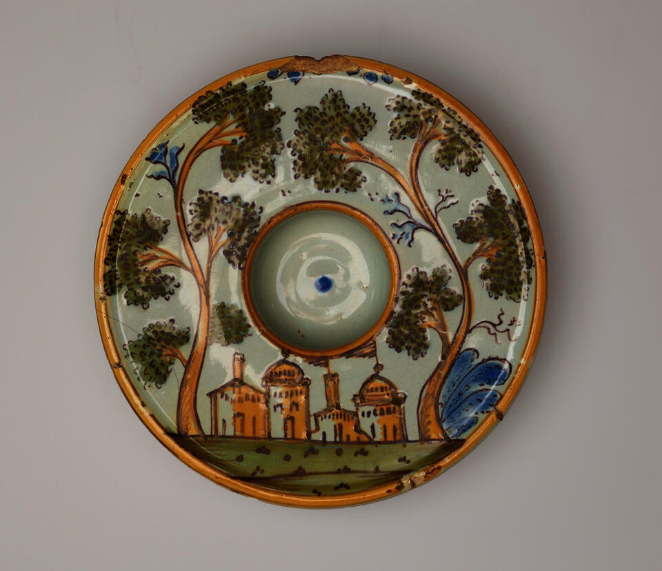 Round plate decorated with an image of buildings and trees. There is a concave well in the center of the form. 