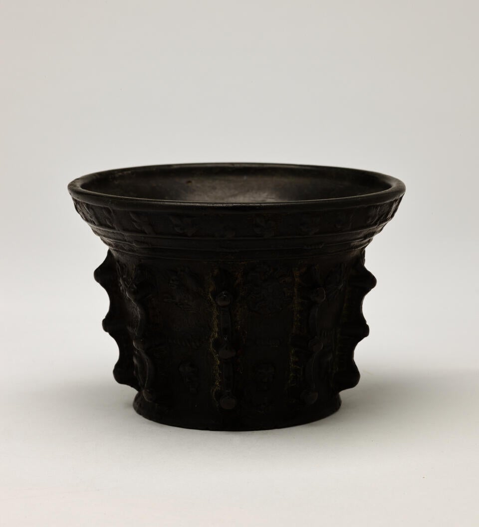 A bronze mortar with protruding decorations on the exterior. 