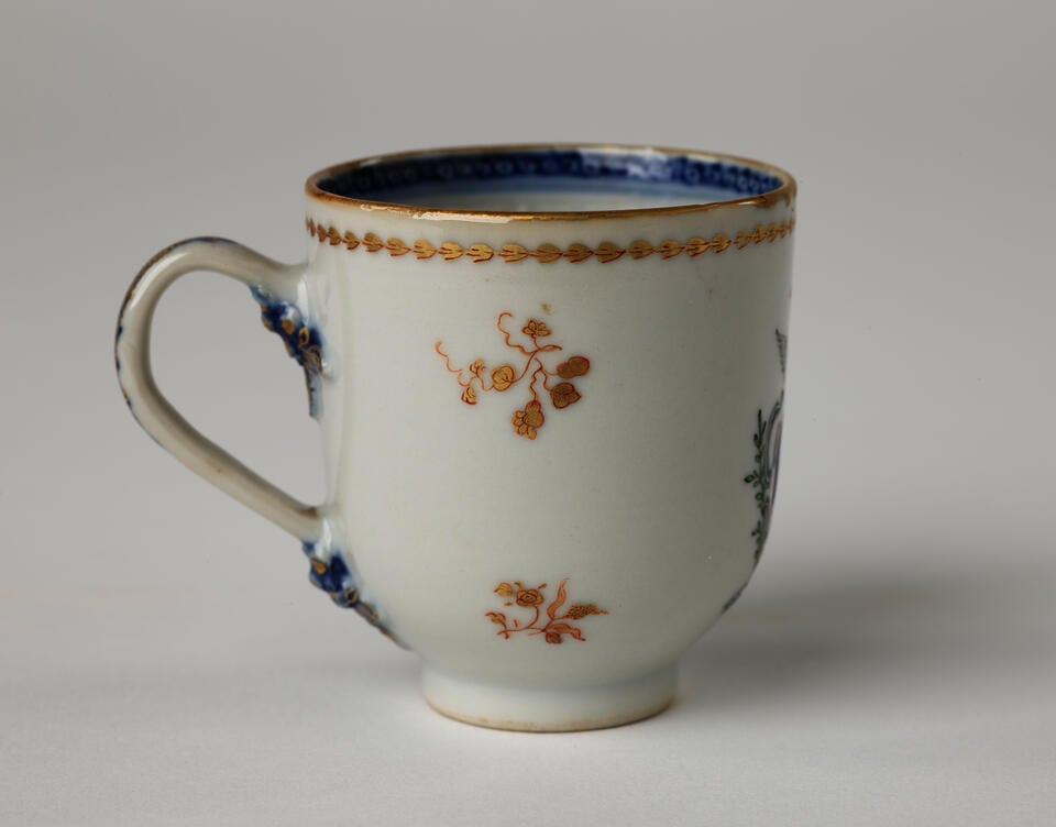 A porcelain chocolate cup with blue and gilded decorations along the outside and inside of the rim, body, and handle. 