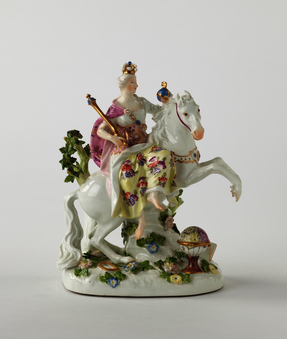 A sculptural figure on a rearing horse in historical clothing that is yellow, pink, and white with floral decorations. The figure is holding a staff and ball.