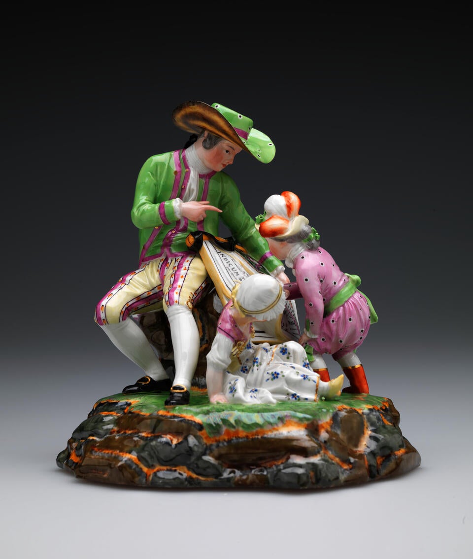 A sculpture with three figures in elaborate historical clothing. A seated light-skinned figure holds a roll of maps while one child examines. A second child sits near them.