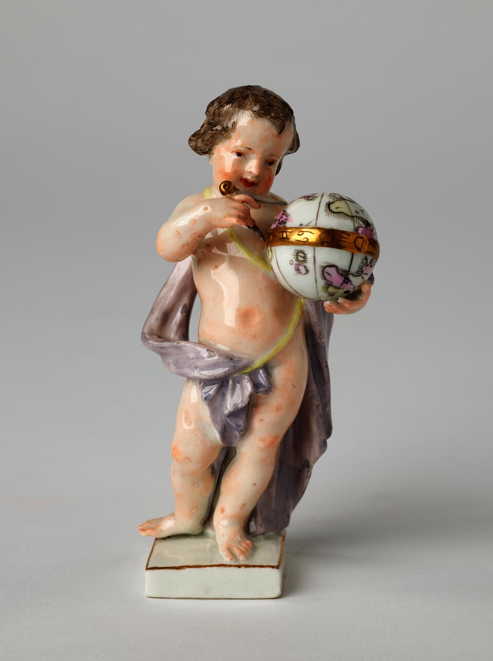A sculptural putto figure holding a globe that is gilded. The putto has brown hair, red lips, and a light purple fabric draped across it. 