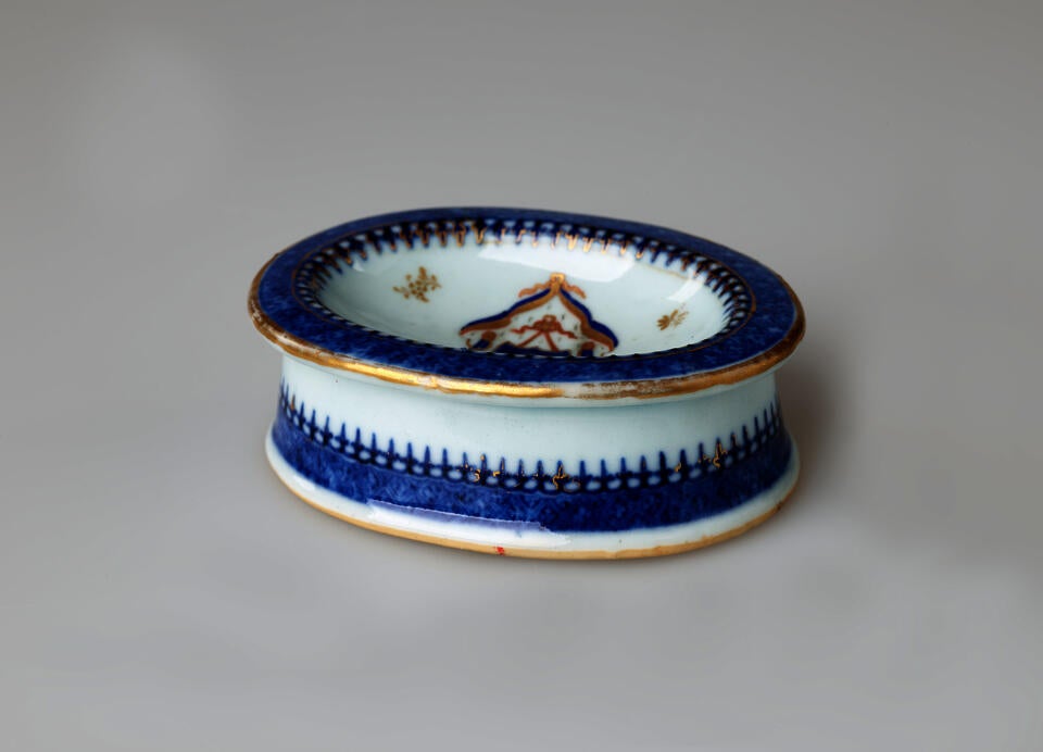 An oval porcelain white salt container with blue and gilded decorations. 