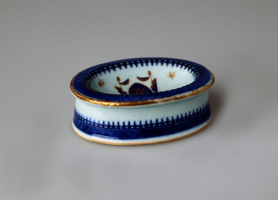 An oval porcelain white salt container with blue and gilded decorations. 