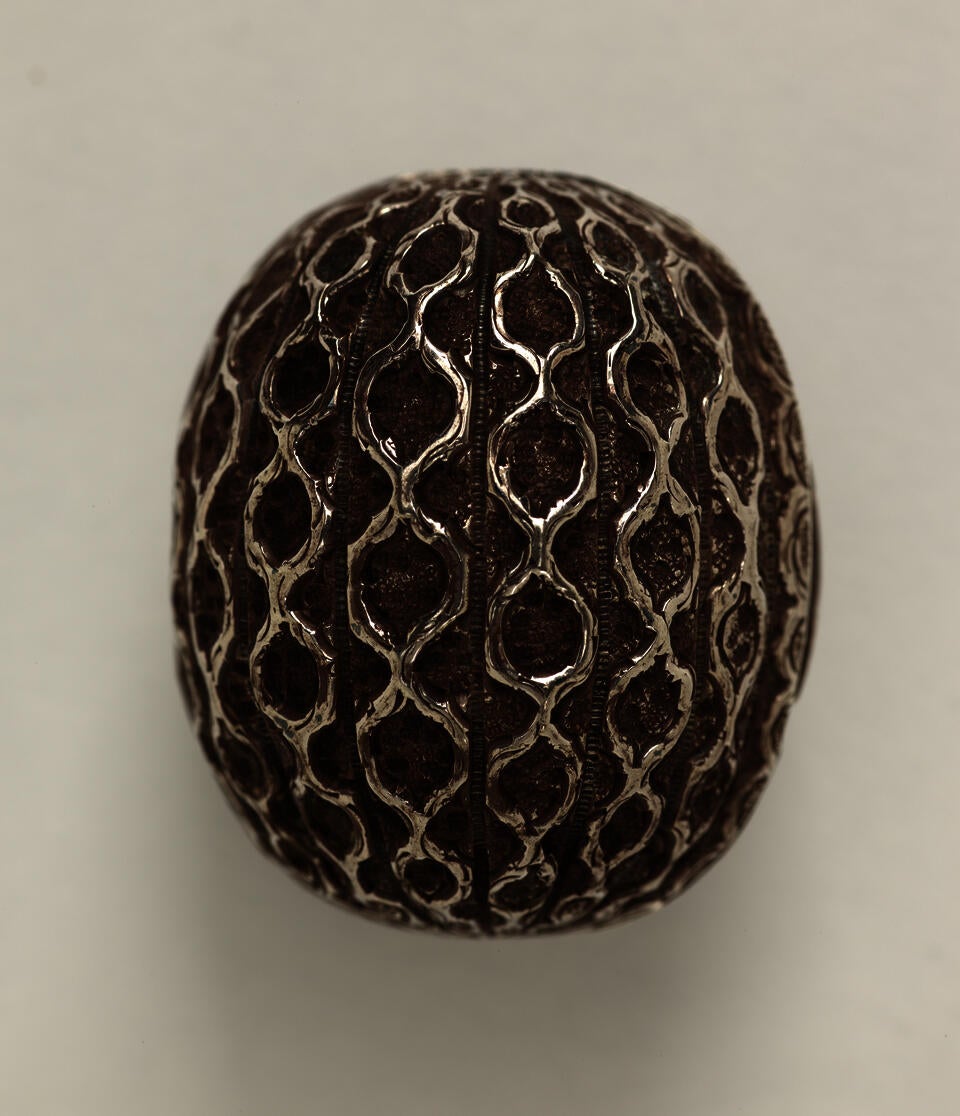 A silver nutmeg grater that is abstractly shaped like a nutmeg seed. 