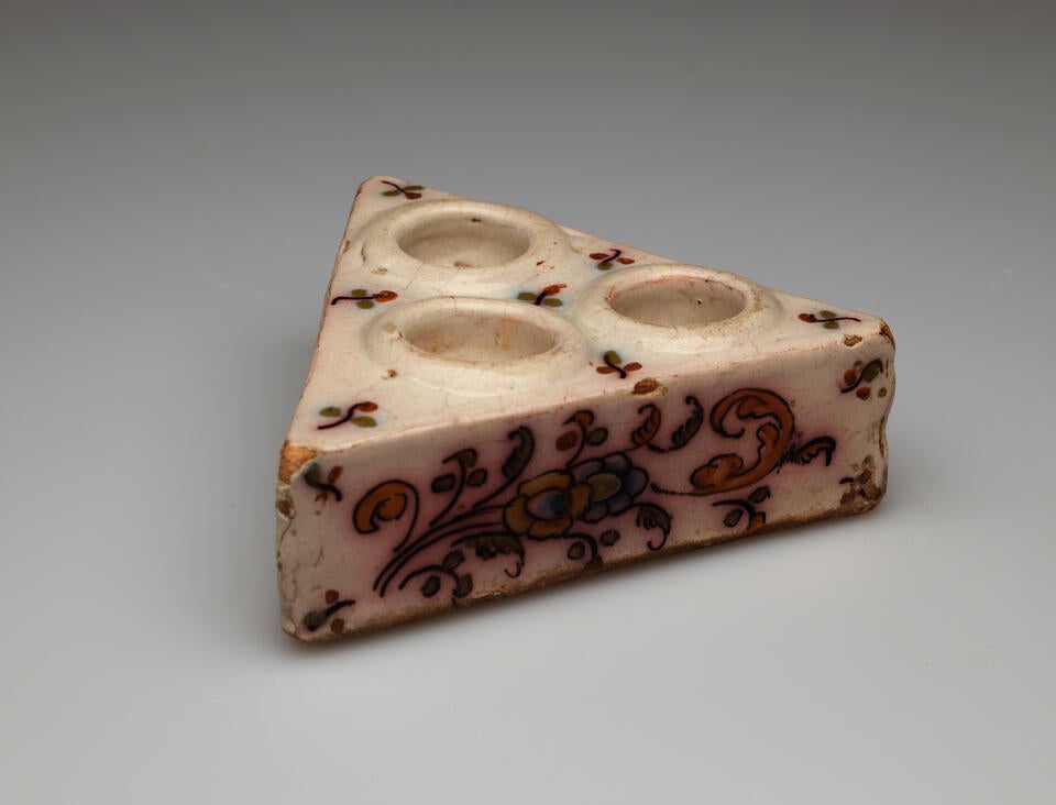 A cream colored triangular salt cellar with three holes on the top with decorative floral decorations.