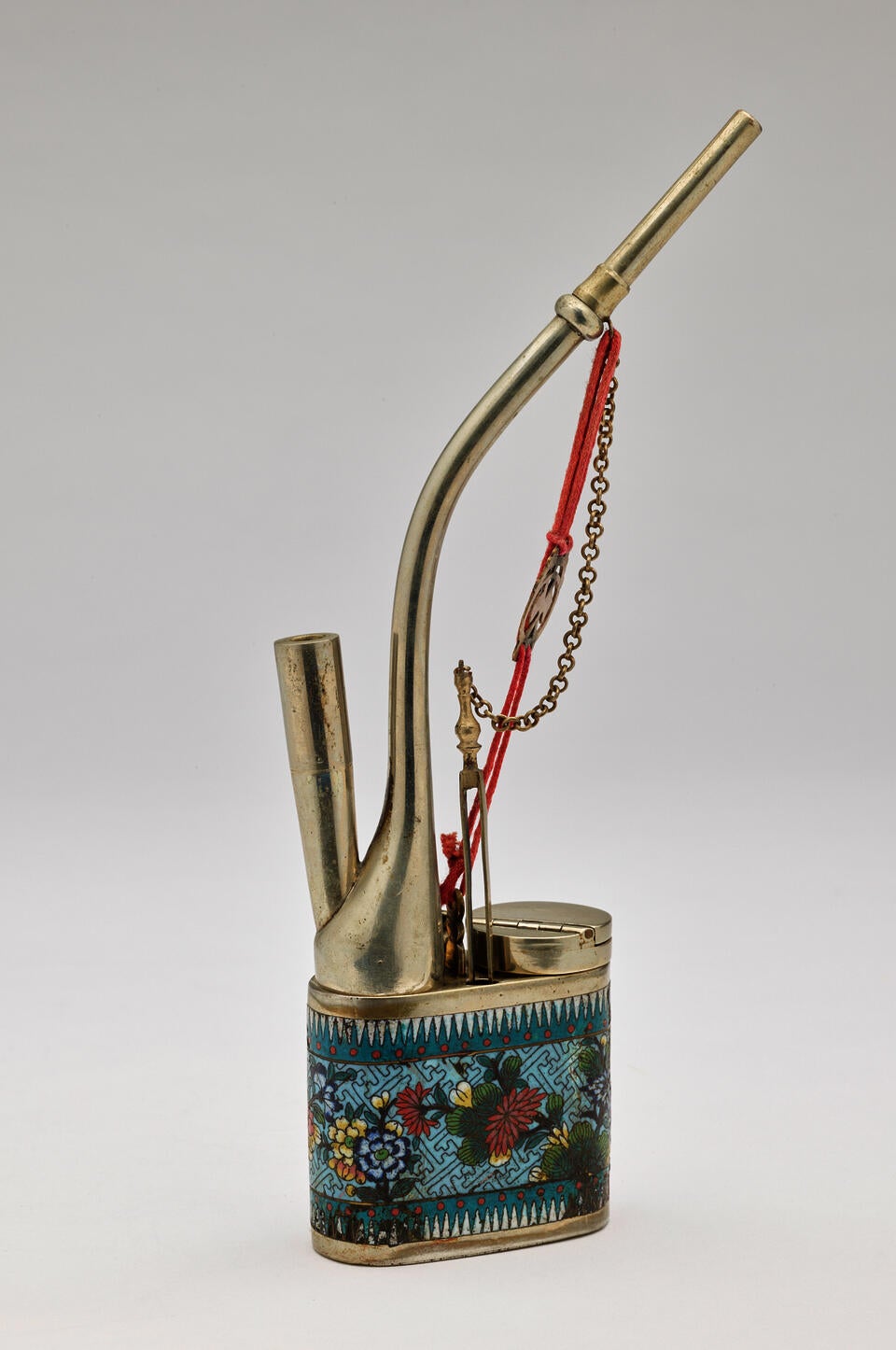 A silver object with blue decoration. A tall, straw-like piece attaches to the square bottom and rises upward, curving left. A red string and chain attach to other silver parts.