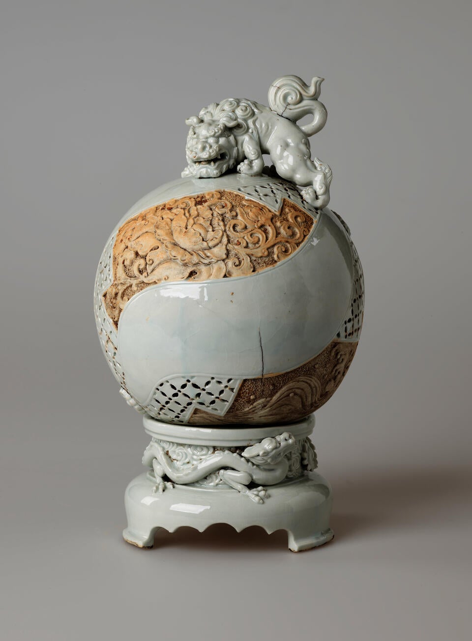 Light-colored sculptural globe with tan sections of ornate carving. An animal figure sits on top of the sphere. The base has a scalloped front edge and image of a dragon.