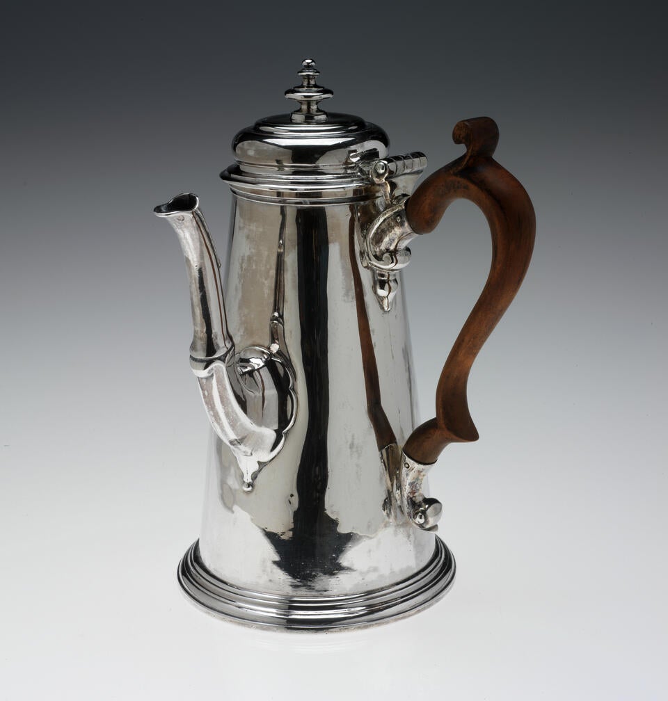 A silver chocolate pot with a spout, hinged lid, and fruitwood handle that is 90 degrees from the spout.