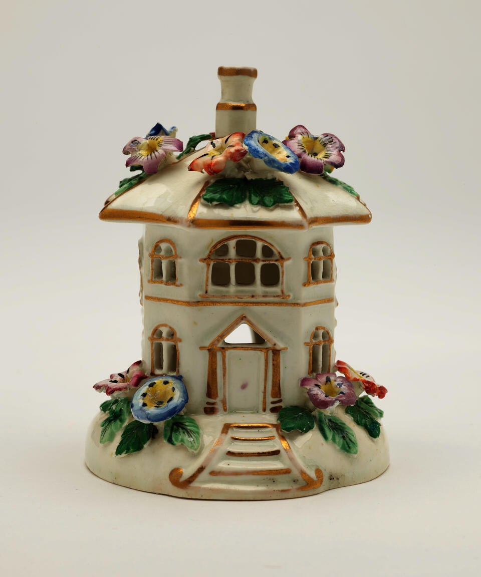 A sculpture in the shape of a small white house, covered in different colored flowers.