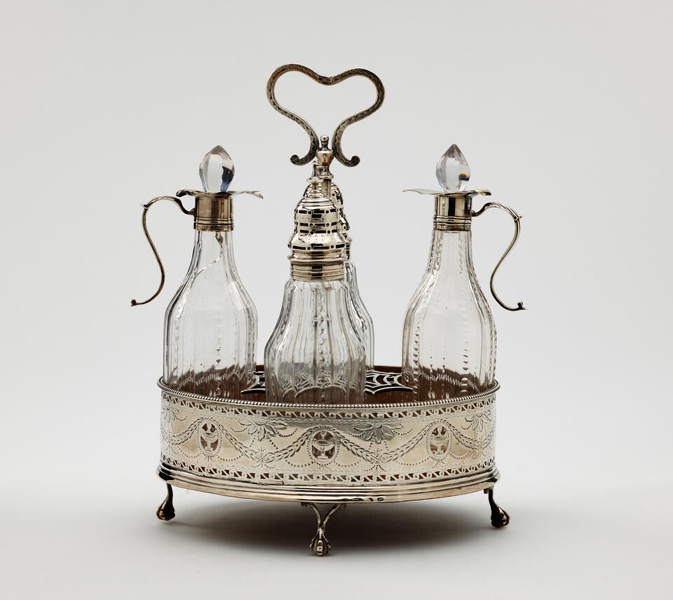 A silver, mahogany, and glass caster set. There are various vessels inside the footed tray. The silver and glass has etched decorations.