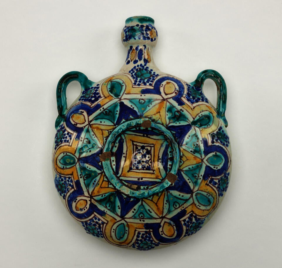 A completely rounded bottle with a neck and two symmetrical handles. There are symmetrical decorations that are dark blue, turquoise, and yellow.