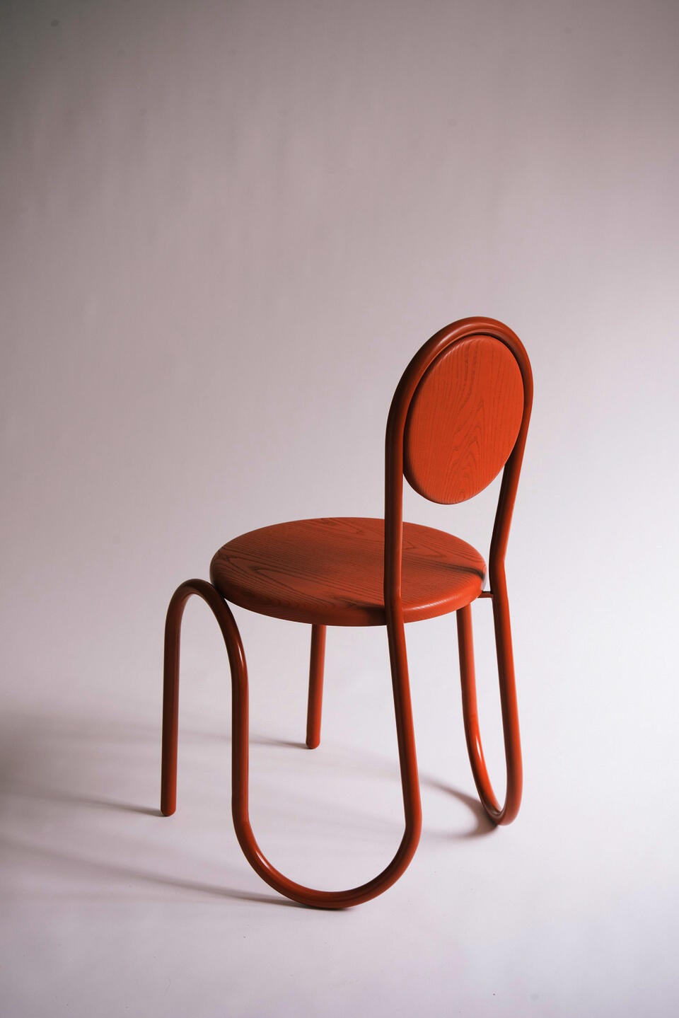 A brown wiggle steel tube chair frame with a wood circular seat and back.