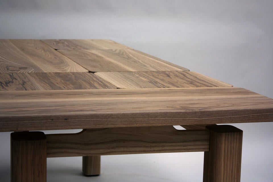 A wooden dining table with a puzzled rectangular top that appears to be floating over the substantial rectangular legs.