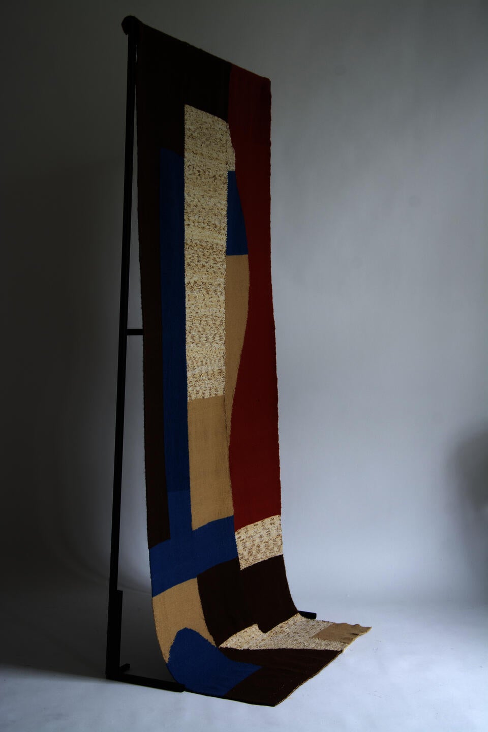 A woven tapestry, made of abstracted cobalt, vermillion, brown and beige shapes.