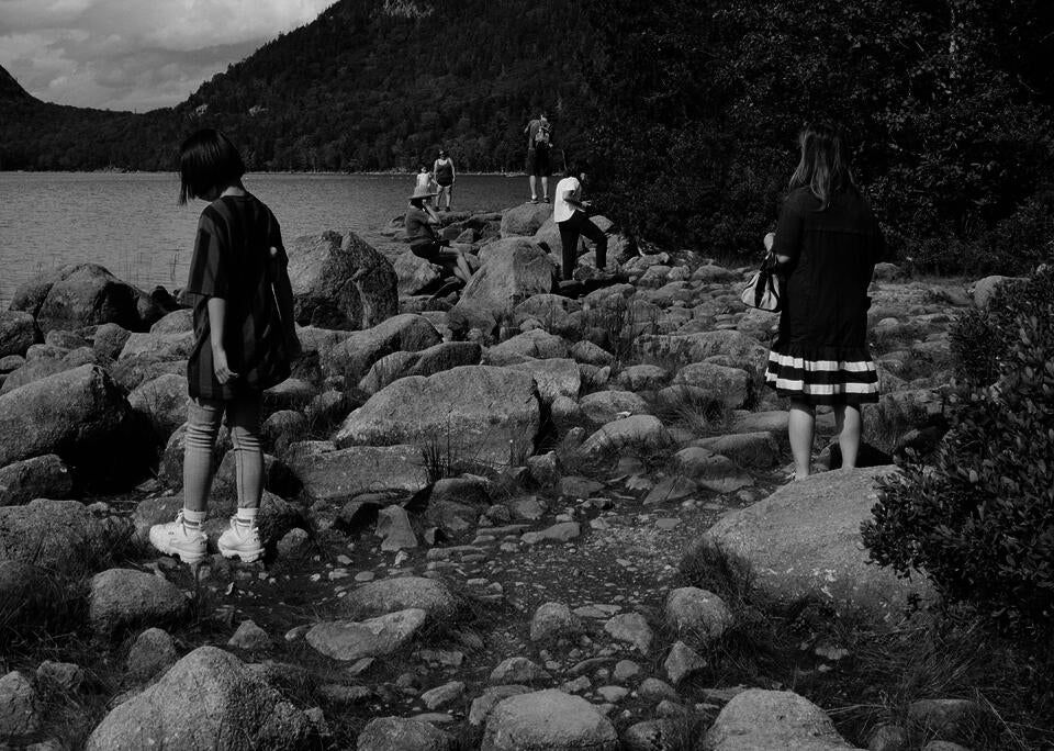 7 people standing in the shape of a triangle on top of boulders at the edge of a lake