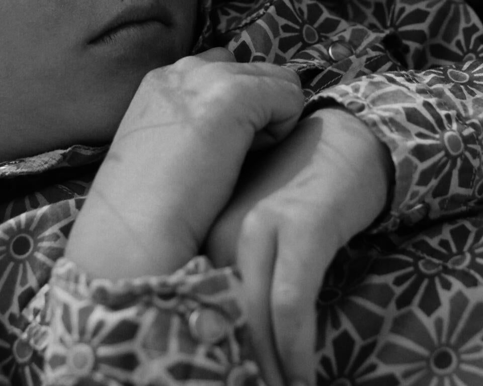 the hands of a young girl resting on her chest, her floral shirt 