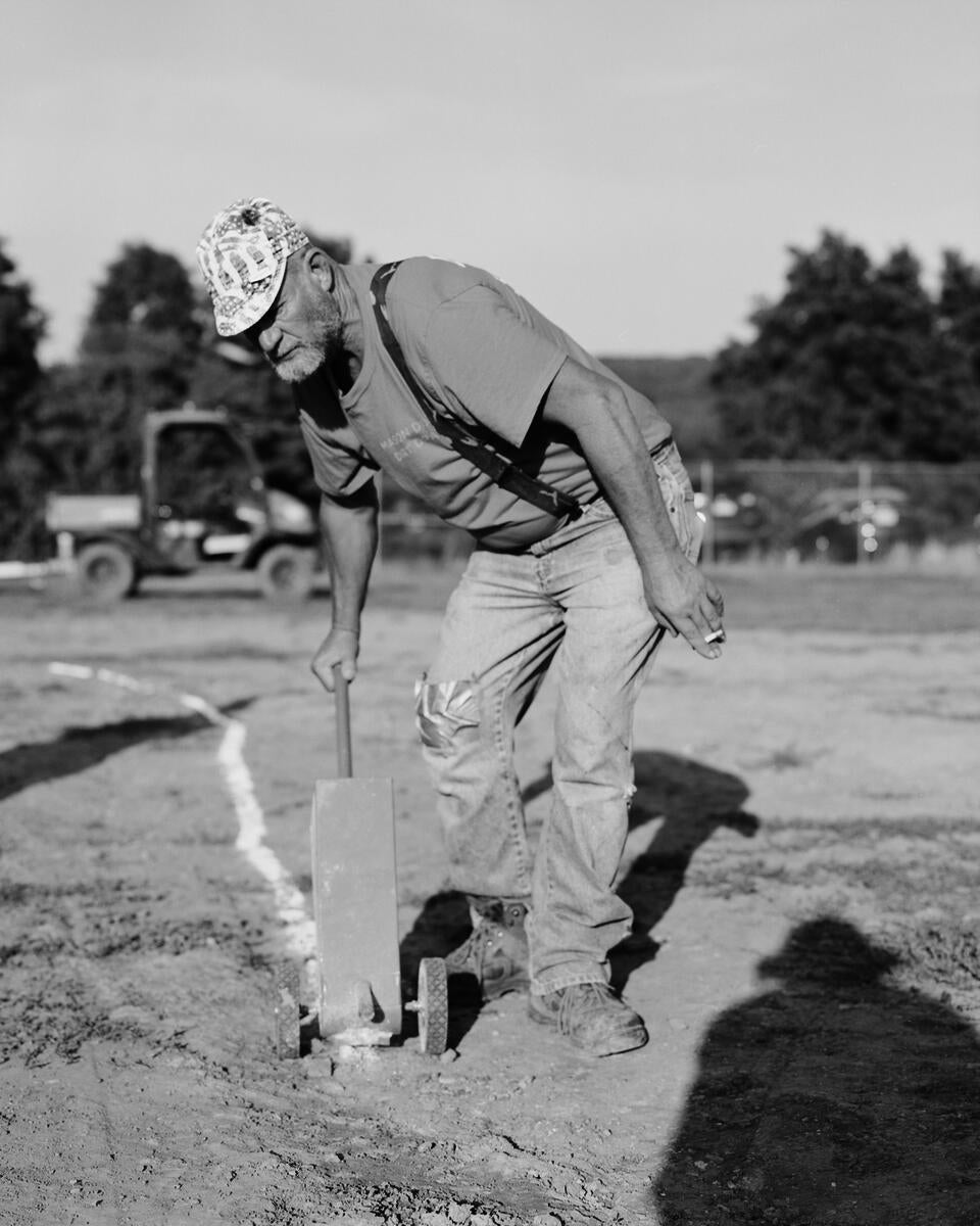 A man in the bright sun drags a chalk line behind him.