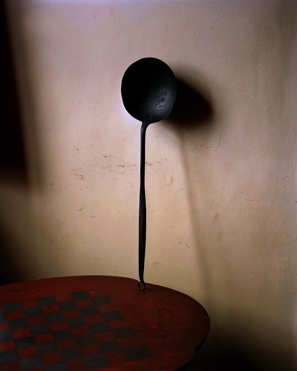 Cast iron cooking spoon standing on top of a small table.