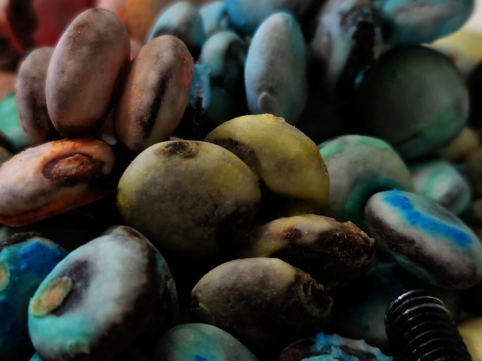 Discolored M&Ms candies on a white ceramic plate, together with screws