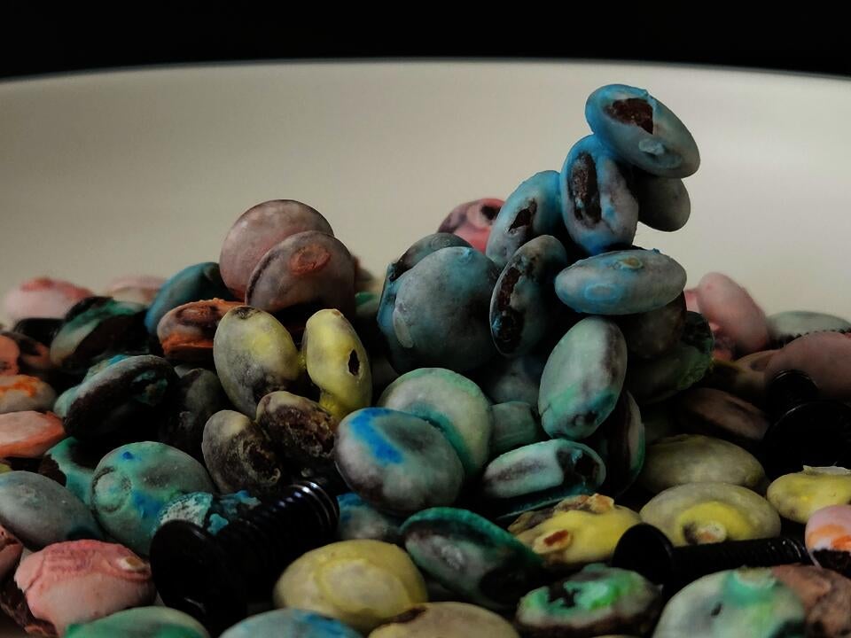 Discolored M&Ms candies on a white ceramic plate, together with screws