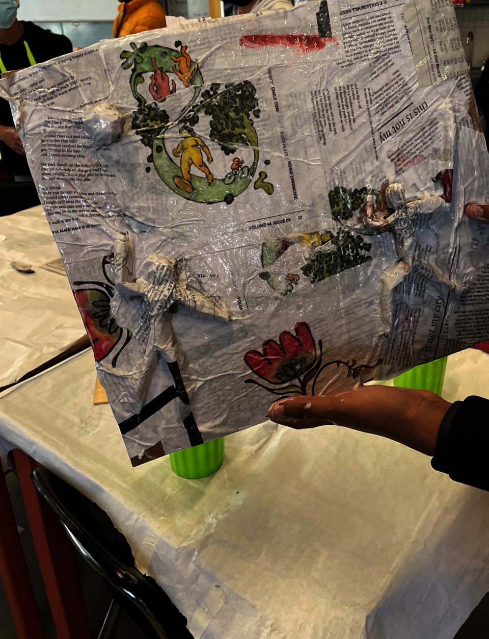 This is a photo of students applying paper maché to their masking tape bases and working together to help a friend!