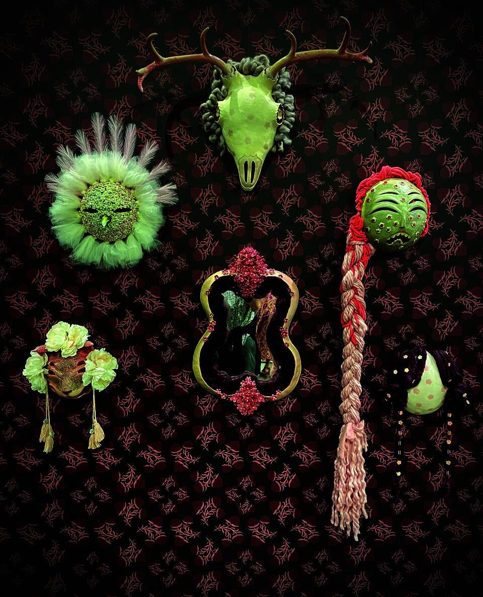 Ceramic masks hang on a wall covered in burgundy floral wallpaper.