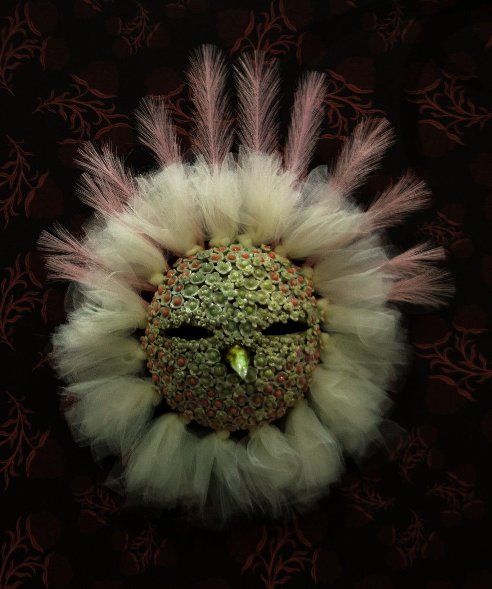 Ceramic bird mask covered in ceramic flowers, ringed in white tulle. 