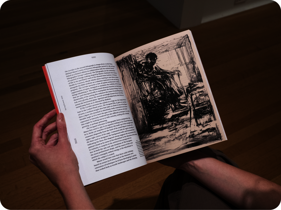 A person holding the book open. The left page features text against a white background while the right page features a black etching of a man in a wheeled chair. 