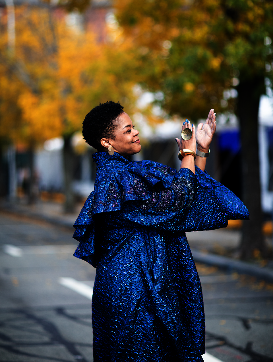A short-haired Black woman in blue ceremonial robes stands outside clapping