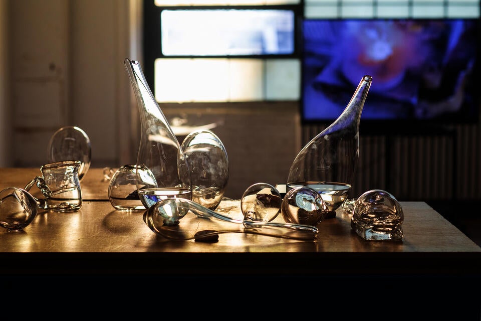 Examples of blown glass vessels sit on a wooden table top.