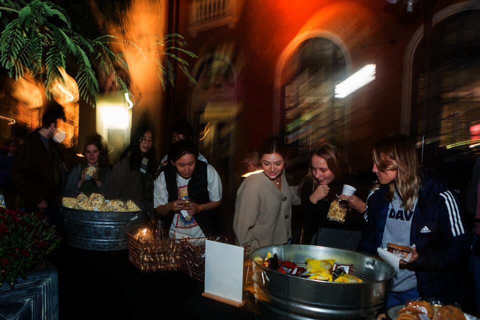 Nighttime photo of several young women looking at a sign in front of a table of snacks.