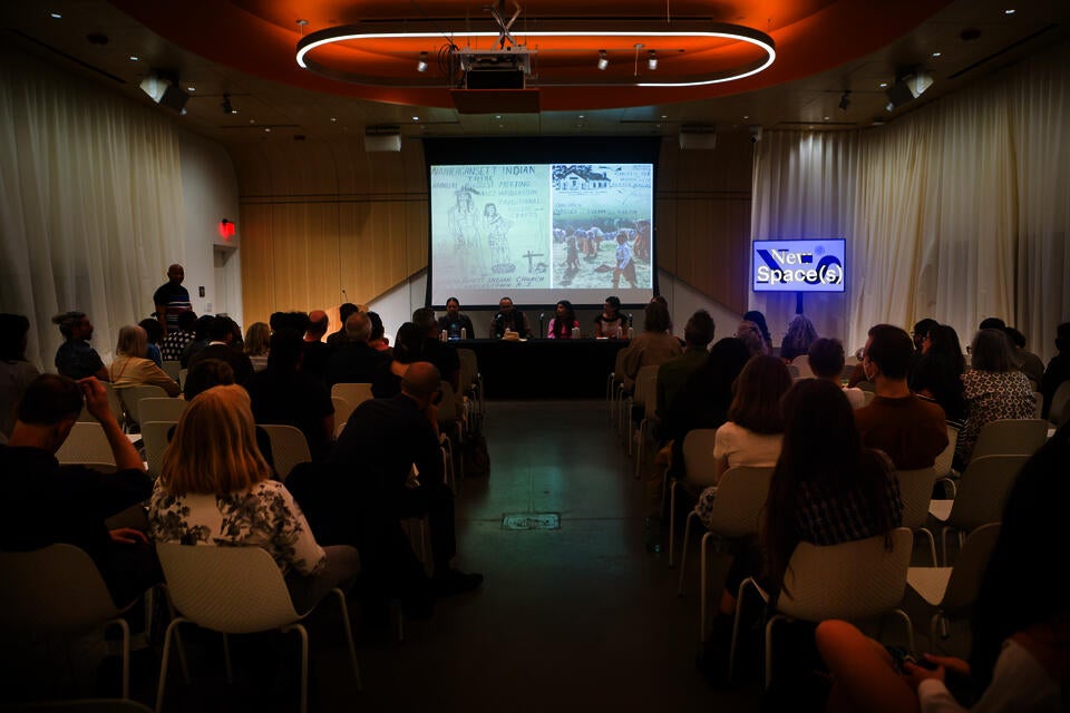Five panelists present to a crowded audience. The projector behind them shows a drawing with handwritten text reading 'Narragansett Indian Tribe Annual August Meeting'