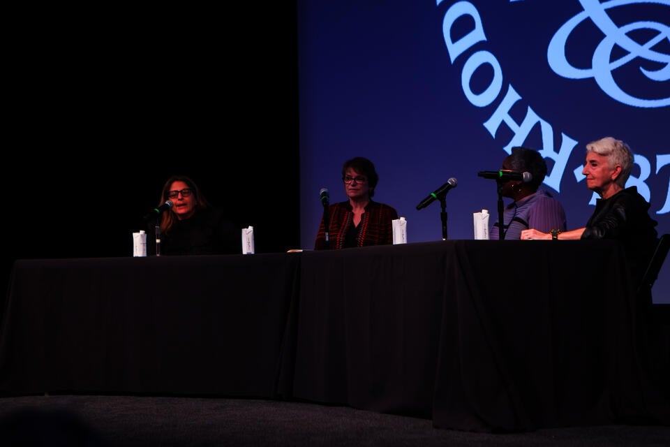 Close-up shot of four women panelists on stage at a table draped in a black cloth.