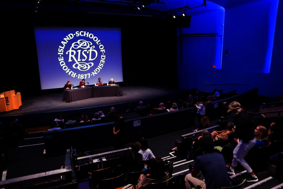 A panel of four people presents in an auditorium. The RISD seal is projected behind them.