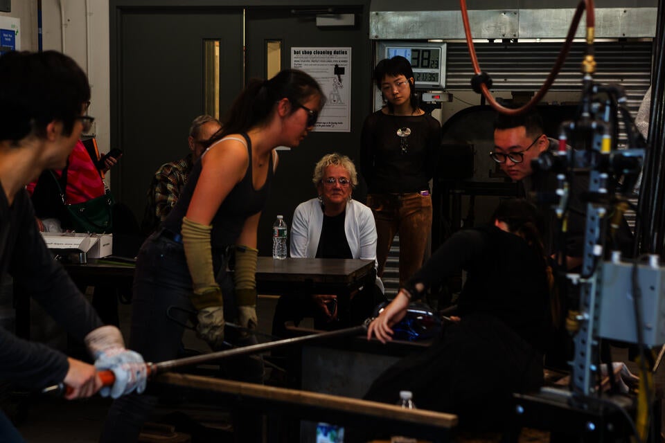 Four students work together in a glass blowing demonstration.