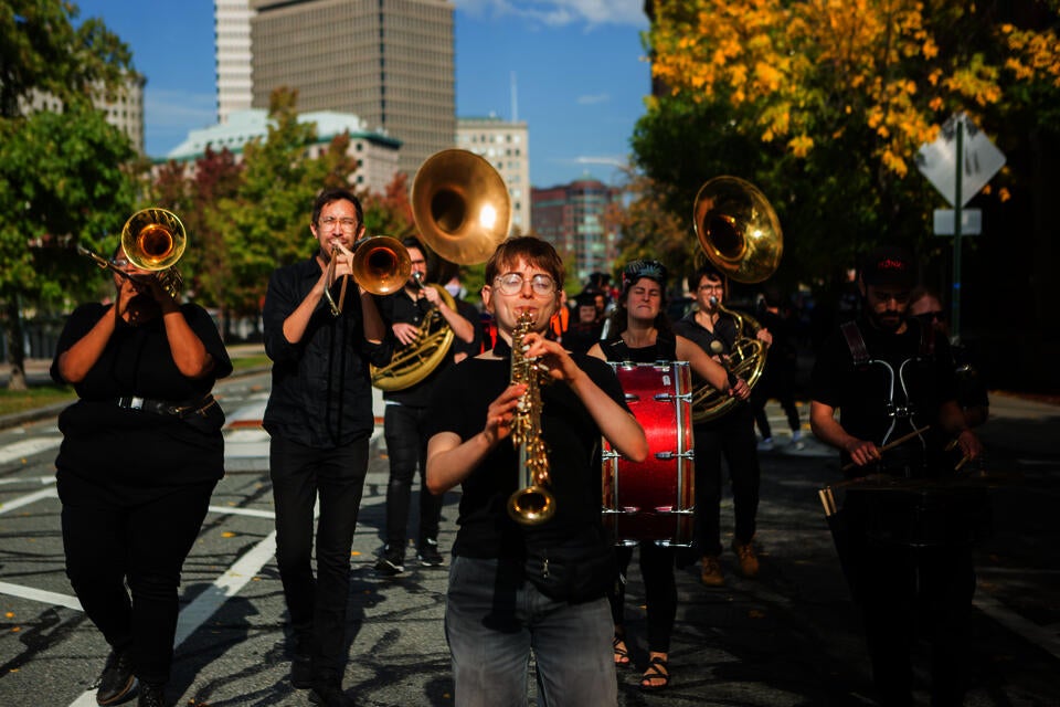 A small brass band walks through a tree-lined street