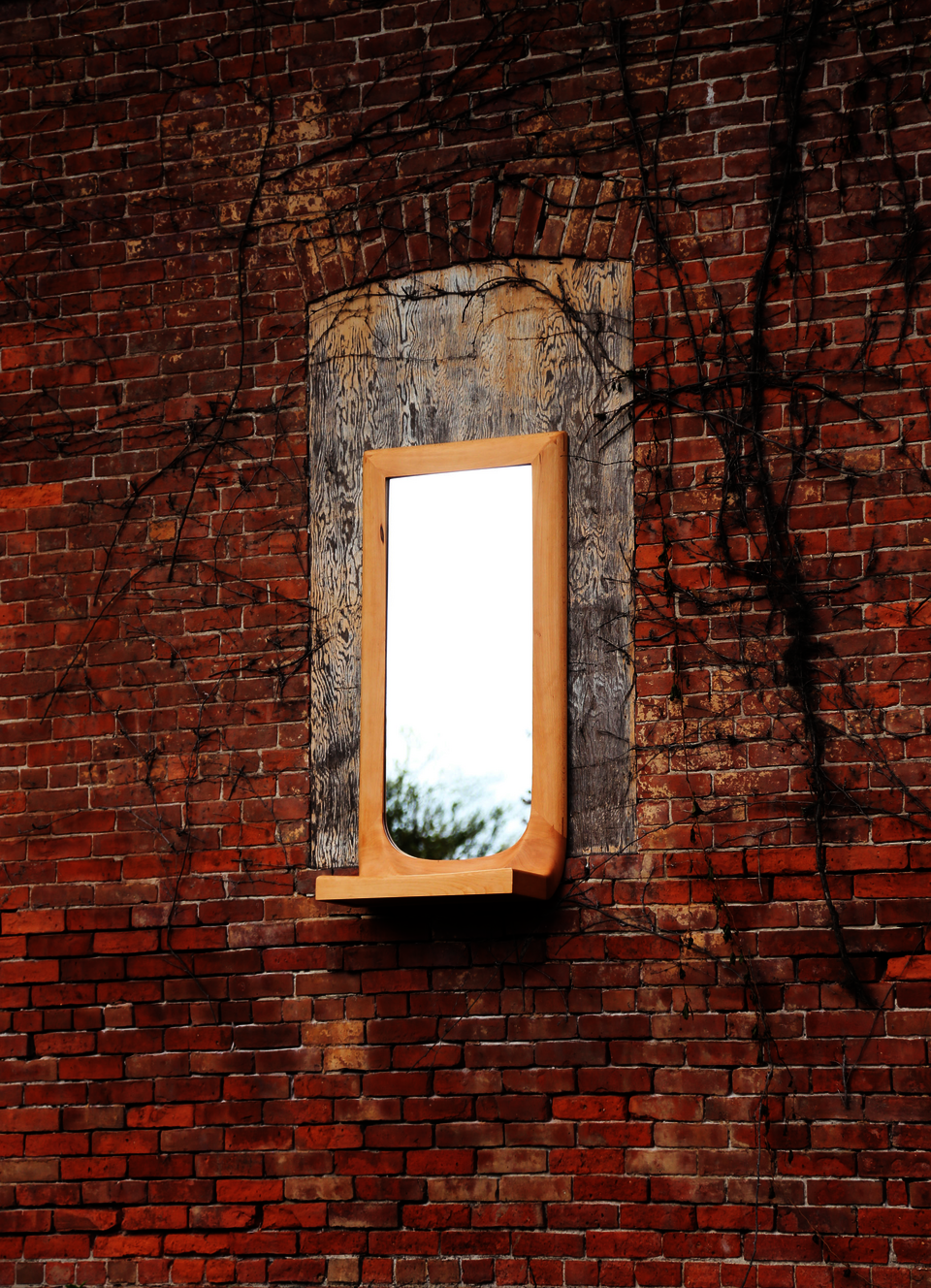 Beech wood mirror with integrated shelf on brick background