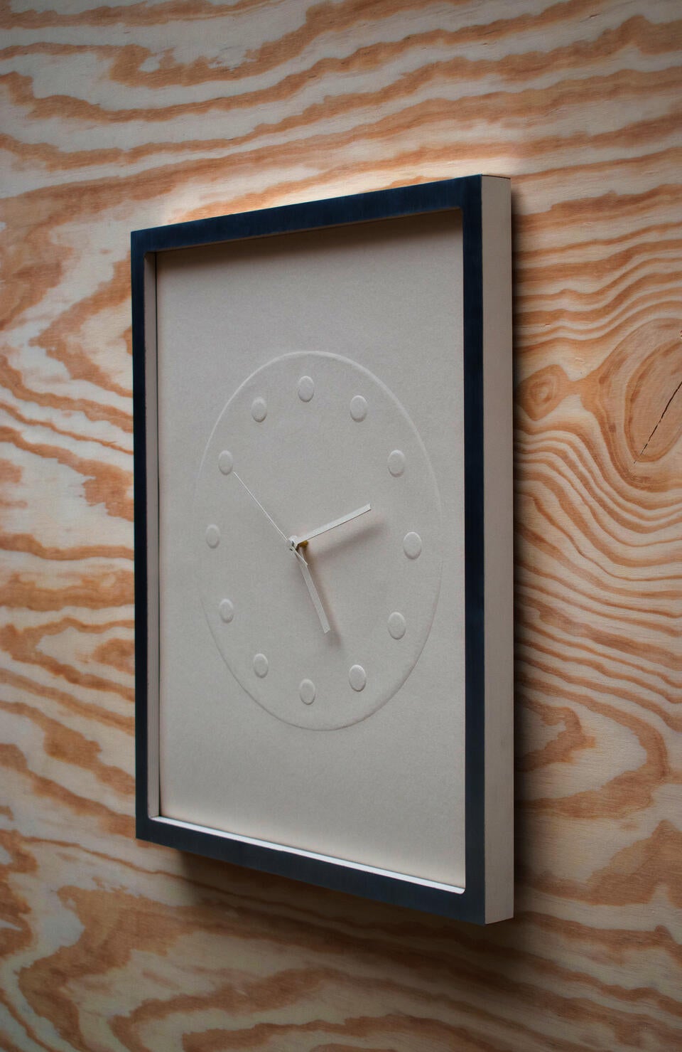 A clock made of embossed paper and presented in a custom frame.
